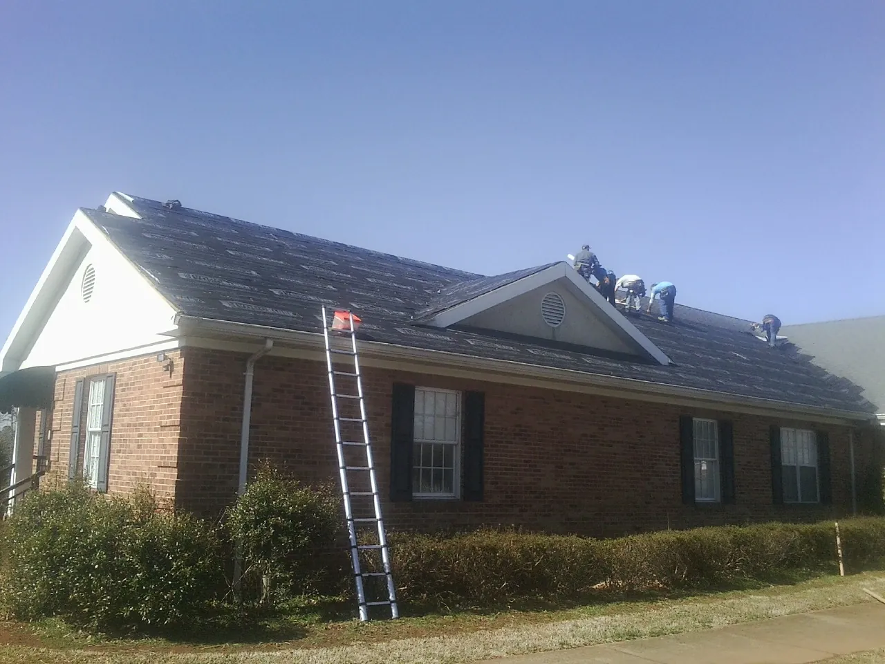Crew tearing shingles off a brick ranch roof with a ladder set — Metal Roof Repair work by our crew in Tiltonsville