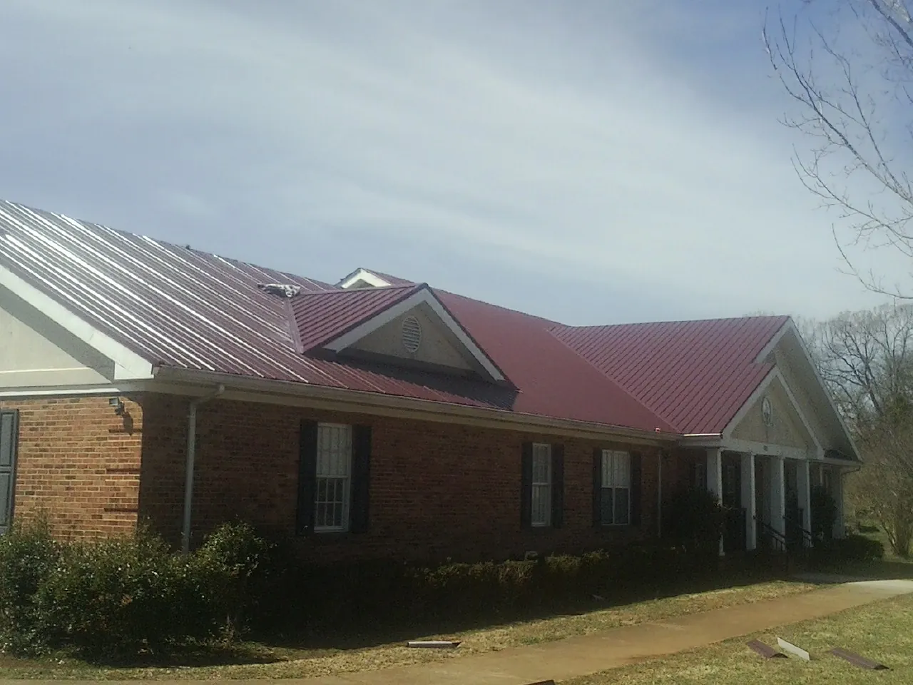 Red metal roof with gabled entries on a long brick building, from a Hail Damage Roof Repair job in Tiltonsville