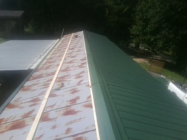 Old rusted panels beside newly installed green metal roofing — Wind Damage Roof Repair by Roofing Brothers in Tiltonsville