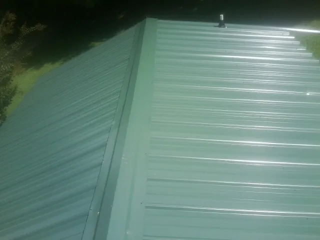 New green metal panels meeting at the ridge of a roof — Flat Roof Repair work by our crew in Tiltonsville