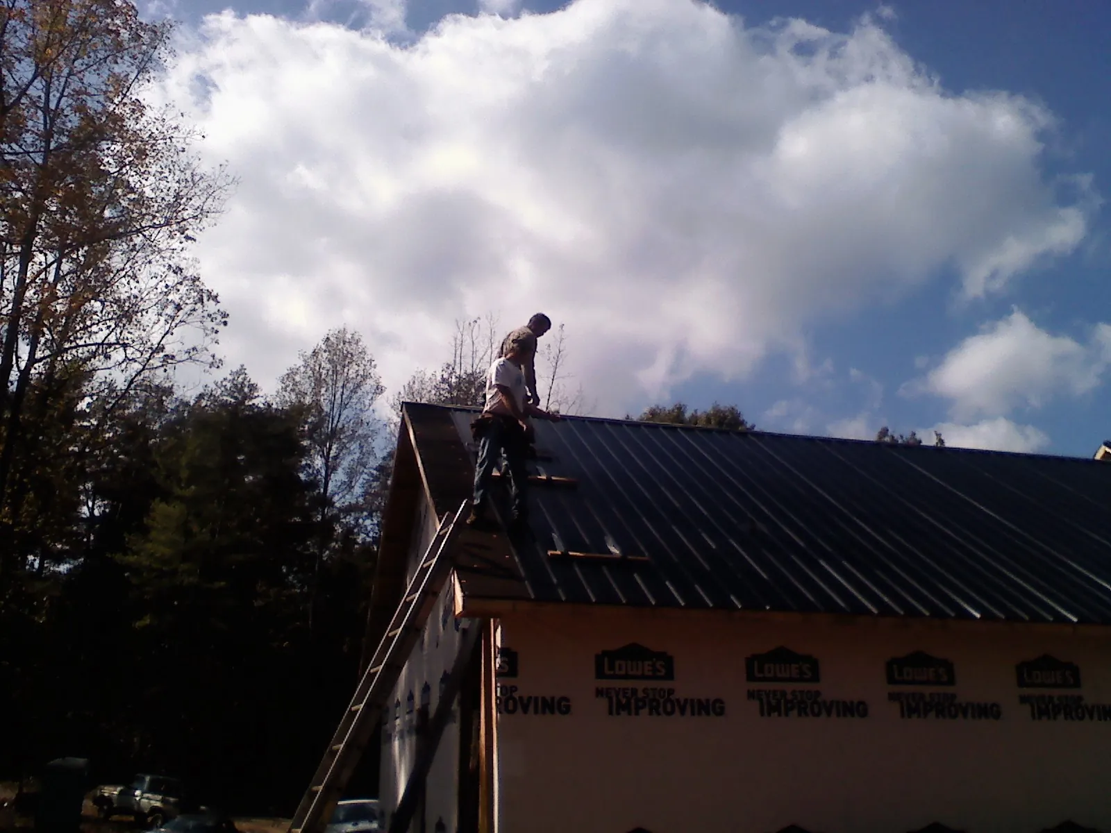 Roofer fastening dark metal panels high against a cloudy sky, from a Roof Inspection job in Tiltonsville