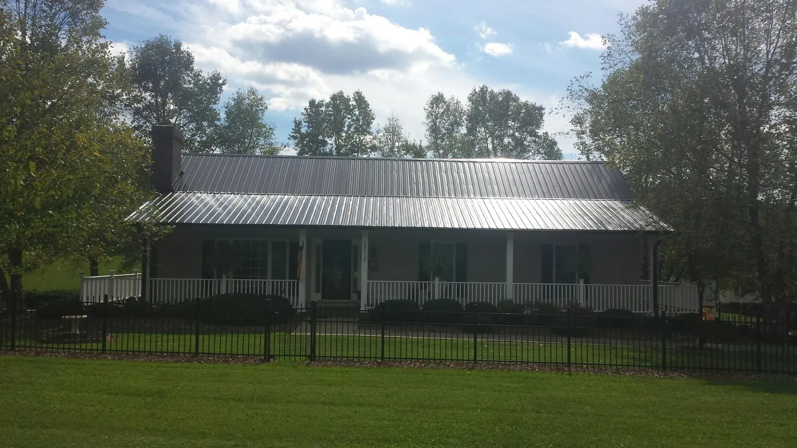 Gray metal roof on a brick ranch with a full width front porch — Gutter Guard Installation work by our crew in Tiltonsville