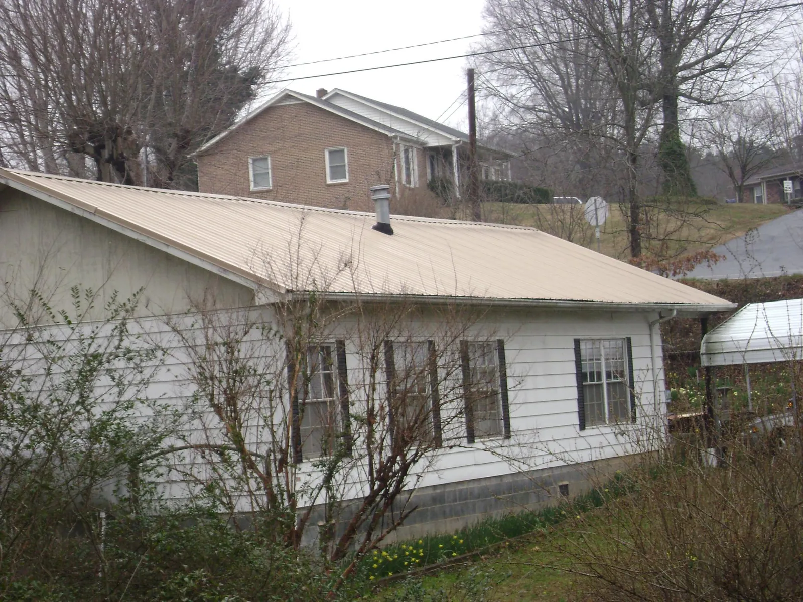 Tan metal roof on a white sided house set into a hillside — Commercial Roofing by Roofing Brothers in Tiltonsville